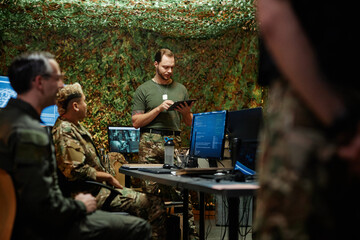 Young man using tablet while standing in front of colleagues in command and control center and...