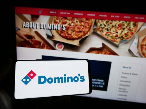 Stuttgart, Germany - 12-09-2023: Person holding smartphone with logo of US restaurant chain company Domino's Pizza Inc. in front of website. Focus on phone display.
