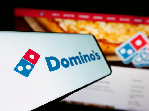Stuttgart, Germany - 12-09-2023: Smartphone with logo of American restaurant chain company Domino's Pizza Inc. in front of business website. Focus on left of phone display.