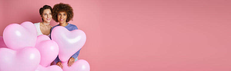 Valentines day banner, dreamy interracial lesbian couple smiling near heart shaped balloons