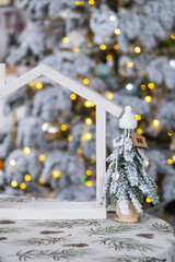 Key on Christmas tree and tiny house on cozy home with Christmas decor on table of festive white kitchen. Gift for New Year. Insurance, moving to new house, mortgage, rent and real estate
