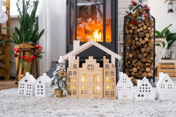 Key on Christmas tree and tiny house on cozy home with Christmas decor near the burning stove fireplace. Gift for New Year. Insurance, moving to new house, mortgage, rent and real estate