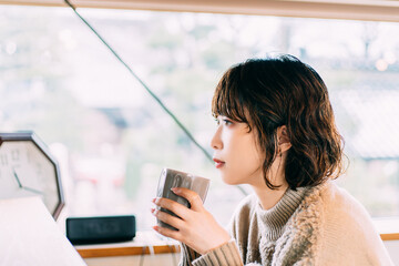 温かい飲み物を飲んで考えごとをする女性