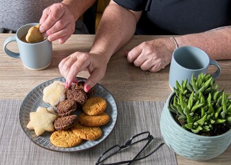 Senior couple with female hand taking cookie and male hand dunking cookie