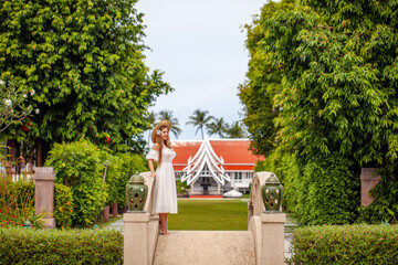 Elegant woman in white dress enjoying leisurely walk in tropical garden. Travel and relaxation.