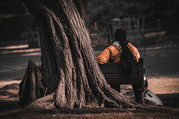 woman sitting on a bench in a park beside an old tree taking in the nature around her, woman relaxing in the nature during daytime