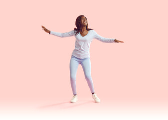 Fototapeta na wymiar Full length portrait of funny afican american girl wearing casual clothes dancing isolated on a pink background. Portrait of a happy young excited woman having fun in studio. People emotions concept.