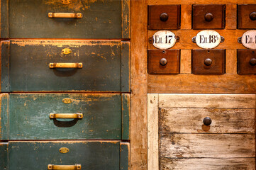 Old wooden drawer fronts in different colors with brass and wooden handles in different shapes. Macro, horizontal photo