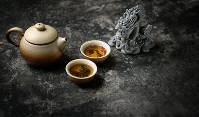 clay teapot, tea cups and dragon figurine on dark table abstract background. Asian culture cuisine...