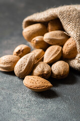 Delicious sweet almonds in wooden bowl or burlap sack on rustic background, roasted almond nut, healthy food