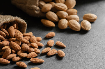 Delicious sweet almonds in wooden bowl or burlap sack on rustic background, roasted almond nut, healthy food