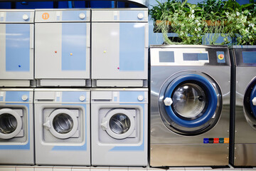 Row of new white and blue washing machines standing next to bigger silver one with green domestic...