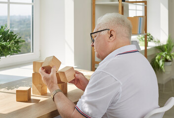 Demented senior man playing puzzle games. Old man with Alzheimer's disease holding wooden cubes in...
