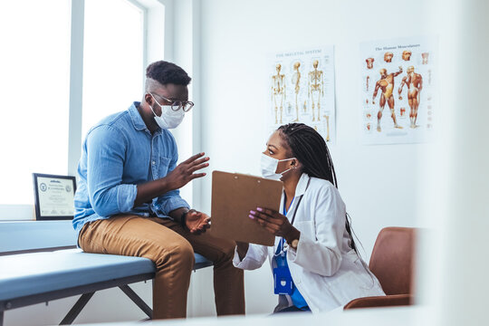 Female Doctor Wearing Face Mask Discussing With Man Patient While Sitting On The Table In The Office At The Hospital. Offering Patient-centered Care That Proves Effective And Efficient