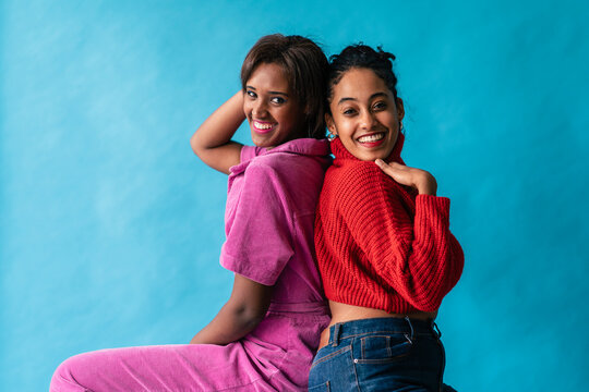 Woman in pink and woman in red sitting back to back with a confident and relaxed demeanor