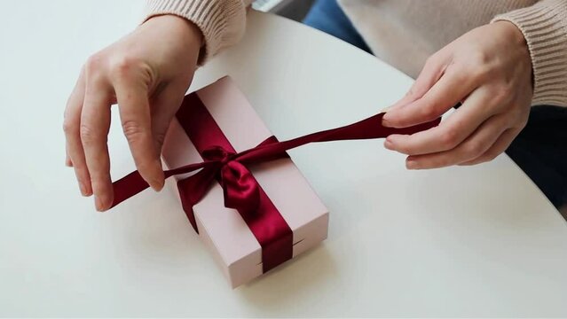 Woman hands unwrapping the gift close up soft pink colors red ribbon