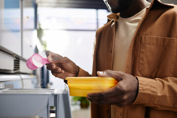 Close-up of young African American man with cap of washing powder pouring it into special...