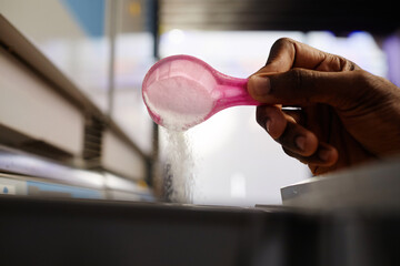 Hand of unrecognizable young African American man pouring soap powder into special compartment in washing machine