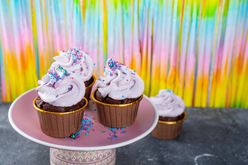 Festive chocolate cupcakes with cream cheese on a background of rainbow tinsel