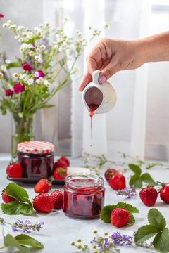 Fresh homemade strawberry jam in glass jar on a light background.