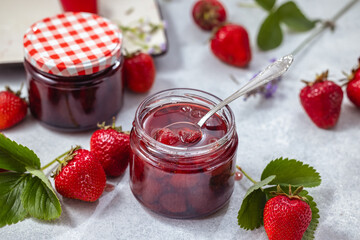 Fresh homemade strawberry jam in glass jar on a light background.
