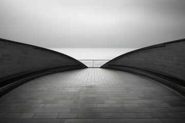  a black and white photo of a walkway with a view of a body of water in the distance and a person...