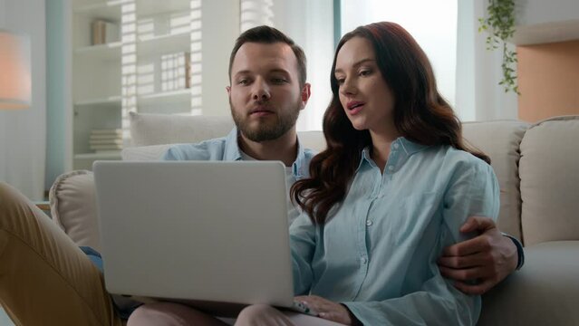 Happy young couple using laptop for ecommerce doing online shopping with shop app together at home Caucasian man and woman looking at computer buying searching in internet booking trip tickets choose