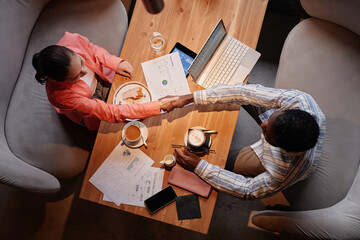 Above view of two successful white collar workers handshaking over table with mobile gadgets,...