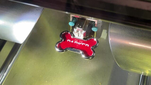 A close up view of a red bone-shaped dog collar getting engraved with the name PARKER.  	