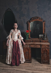 Beautiful woman in rococo style medieval dress standing near console mirror table