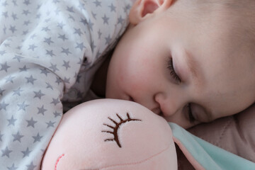Baby with pink bunny soft toy. A girl of European appearance, wearing a light light jumpsuit, is sleeping in the crib. Sleep schedule, care and hygiene of a child up to one year old.