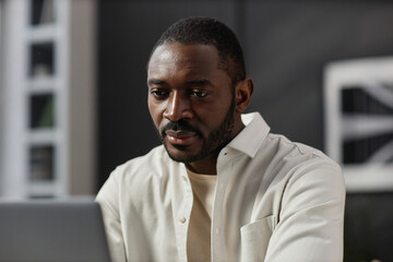 Portrait of adult African American man looking at laptop screen while working at home office, copy space