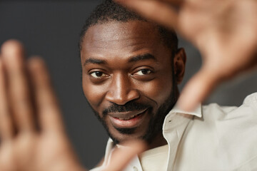 Closeup portrait of smiling African American man looking at camera through hands, copy space