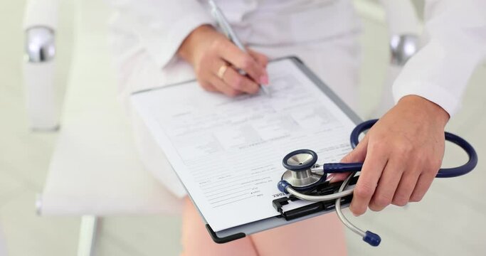 Doctor hand with pen writes medical report on clipboard in hospital