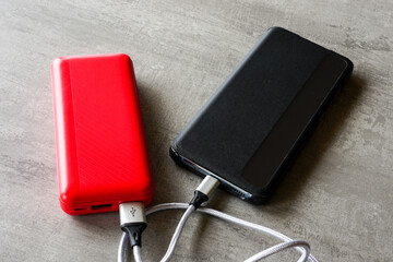 Modern black smart phone charging with help of red power bank, powerbank charges the phone
