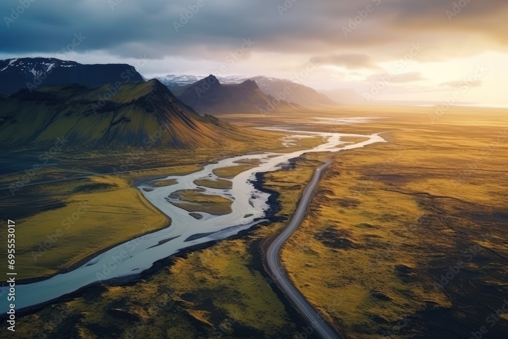 Poster an aerial view of a river running through a valley with mountains in the background and a cloudy sky