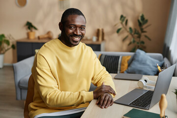 Portrait of smiling adult Black man looking at camera sitting at home office workplace, copy space