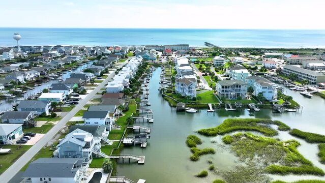 Aerial push in shot toward the ocean over a coastal canal with homes, docks, and boats at Ocean Isle NC.