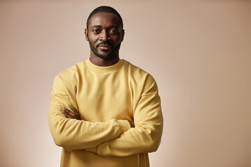 Minimal portrait of confident Black man looking at camera in studio standing with arms crossed against neutral background, copy space