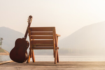 The wooden guitar was set up beside a chair on a wooden balcony in the morning over a reservoir...