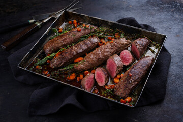 Traditionell gebratenes Rehrückenfilet mit Mangold, Karotten und Kräuter serviert als Nahaufnahme auf einem rustikalen Metall Tablett