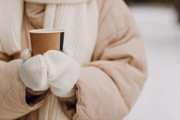 Female hands holding coffee hot drink cup and enjoys winter weather at snowy street close up