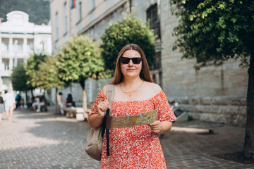 Portrait beautiful woman in sunglasses with paper map in street. Happy tourist travels in Europe. Vacation concept by exploring interesting places to travel. Women Searching locations at summer day.