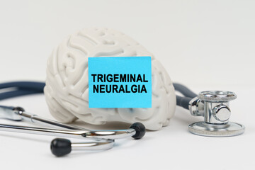On a white surface next to the stethoscope lies a brain on which a sticker with the inscription - Trigeminal neuralgia