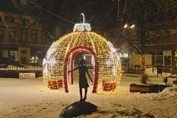 A figurine of a girl against the background of Christmas Illumination in the form of a ball on the...