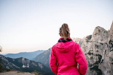 View from behind of a female hiker in pink jacket standing looking at beautiful mountain view