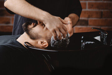 Hairdresser use shampoo for washing hair of man in barbershop. Concept spa cosmetic for head men in...