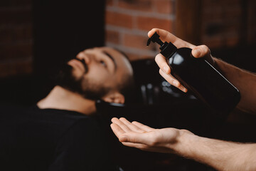 Mockup dark shampoo bottle on background of man in barbershop washing hair. Concept spa cosmetic for head men