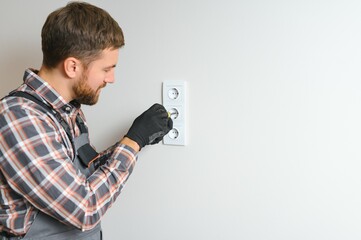 Confident professional electrician in uniform using screwdriver while replacing a socket in apartment after renovation work.