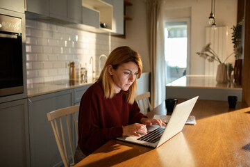 Concerned woman reviewing documents while working from her home kitchen